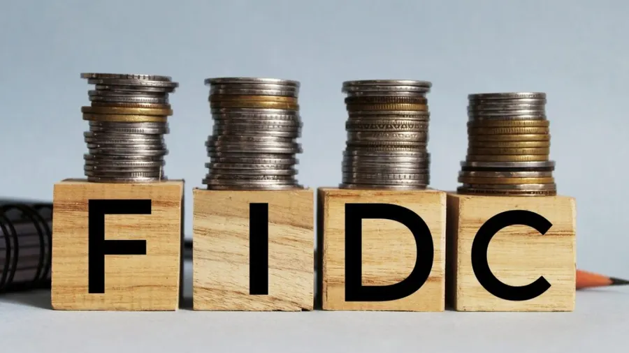 Blocos de madeira formando a sigla FIDC com pilhas de moedas sobre eles